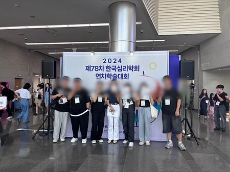 학생들이 “2024 제78차 한국심리학회 연차학술대회"라고 쓰인 벽 앞에서 프로그램북을 들고 있다.